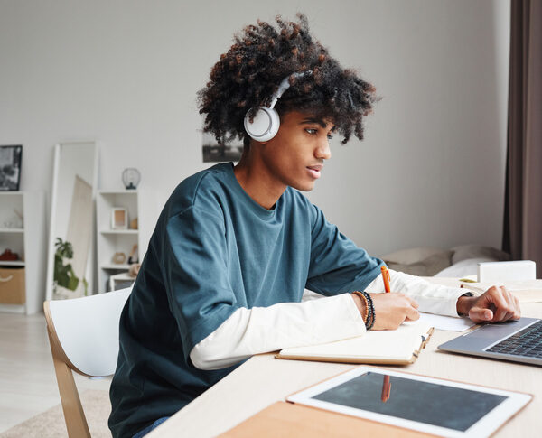Side view portrait of African-American teenage boy studying at home or in college dorm and using laptop, copy space