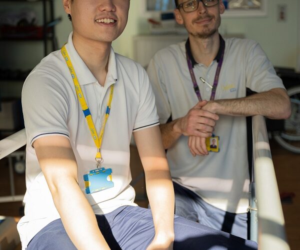 Two masculine presenting people with yellow and purple Oxleas lanyards looking at the camera