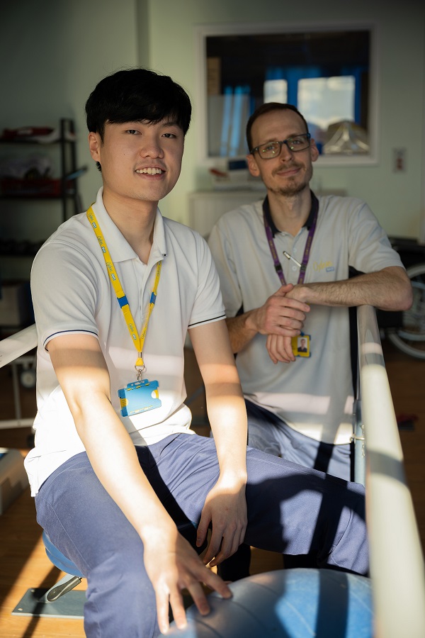 Two masculine presenting people with yellow and purple Oxleas lanyards looking at the camera