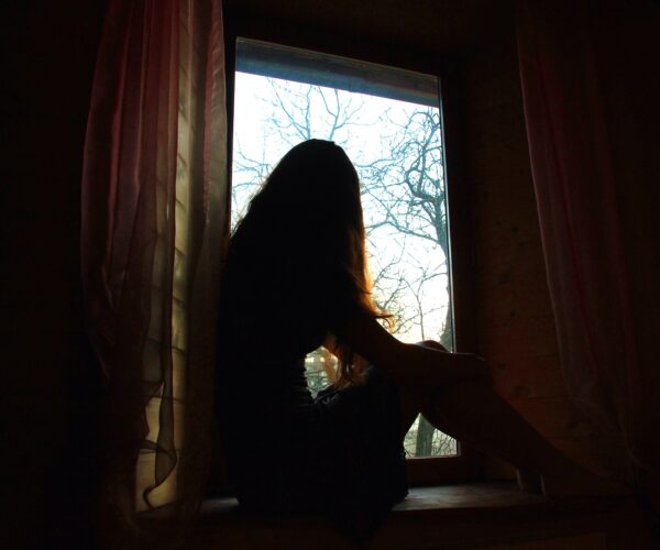 A girl sitting in a dark room, looking out a window